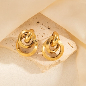 Detailed close-up of intertwined golden hoop earrings on a beige stone surface