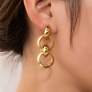 Close-up of golden geometric double-loop earrings on a model showing shiny metal texture