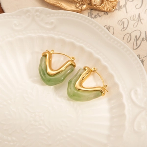 Elegantes pendientes en V dorados con resina verde claro sobre un plato de cerámica retro