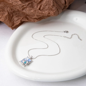 Détail d'un pendentif floral rectangulaire avec incrustation bleue sur chaîne fine
