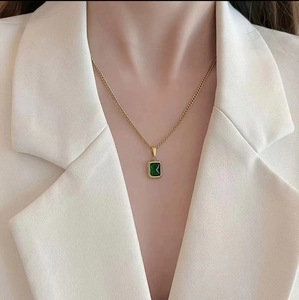 Elegant gold titanium necklace with a square green gemstone worn by a model in a beige suit
