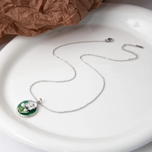 Détail du pendentif muguet en émail vert et perles sur une fine chaîne en métal argenté