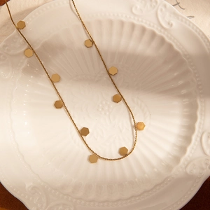 Detail of a gold choker necklace with hexagon pendants in a white relief ceramic bowl