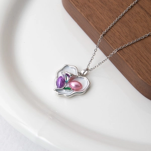 Détail d'un pendentif cœur avec perles et feuille verte sur une chaîne en acier