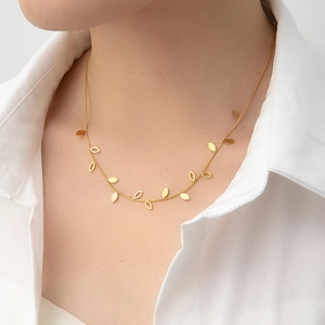Detail of elegant gold butterfly necklace with hollow leaf charms on white shirt