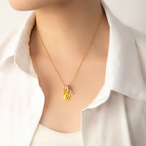 Detail of gold chain necklace featuring yellow flower and purple ring pendants on a model