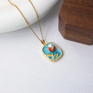 Détail du pendentif en émail doré orné d'une tulipe rouge et d'une perle blanche centrale