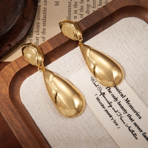 Elegantes pendientes de gota dorados con textura martillada en bandeja de madera retro