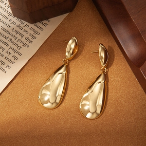 Detalle de pendientes de gota bañados en oro de 18k sobre papel vintage y madera