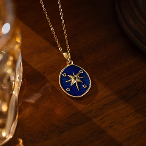 Detail of golden starburst pendant with blue enamel and green gems on a wooden background