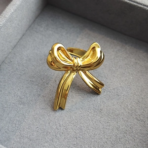 Polished gold ribbon bow ring in textured stainless steel with an adjustable open band design