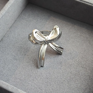 Polished silver ribbon bow ring made of stainless steel inside a gray velvet jewelry box