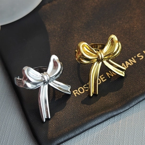 Polished gold and silver ribbon bow rings set on a textured black leather background