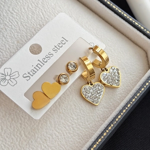 Macro detail of stainless steel heart earrings and round zircon studs on white card