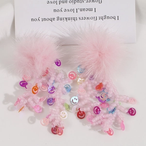 Dettaglio di orecchini con pompon in pelliccia rosa e nappe di perline con faccine