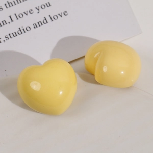 Macro detail of glossy light yellow heart resin earrings on a minimalist background