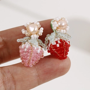 Dettaglio macro di orecchini a fragola fatti a mano con piccolo fiore bianco e perla