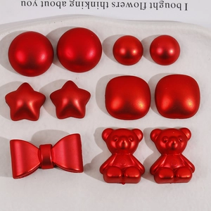 Macro view of red star, bow, and bear-shaped acrylic DIY accessories on a white tray