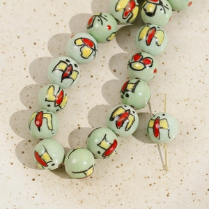 Macro detail of 12mm mint green ceramic beads with hand-painted butterfly floral patterns