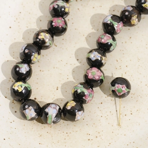 Detailed macro view of 12mm black hand-painted ceramic beads with floral patterns and pins