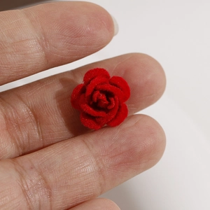 Close-up of a small red flocked velvet rose flower held between fingers for size