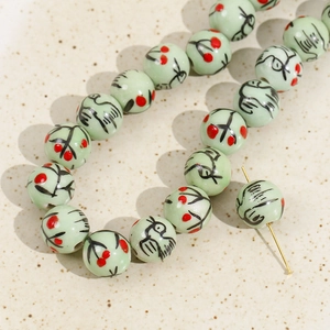 Macro view of 12mm light green ceramic beads with hand-painted floral motifs for DIY jewelry