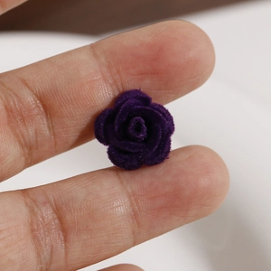 Close-up of a tiny purple flocked rose petal charm held on a fingertip for DIY crafts