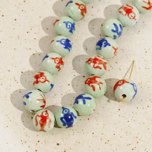 Macro detail of 12mm ceramic beads with hand-painted red and blue fish patterns