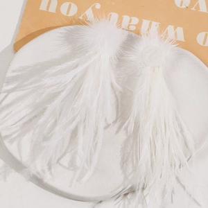 Detailed view of elegant white long feather accessories with fuzzy pom poms on a ceramic plate