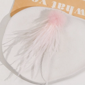 Close-up of a soft pink feather accessory with a fluffy pompom on a stone pedestal