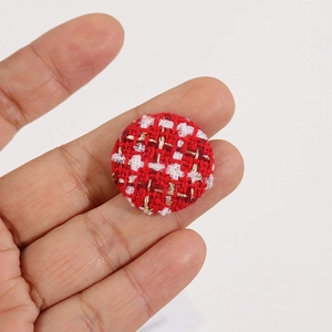 Vue détaillée d'un bouton en tweed rouge de 25mm tenu entre les doigts pour projets DIY