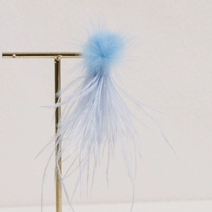 Detailed view of light blue ostrich feather and fluffy fur pompom accessory on a gold stand