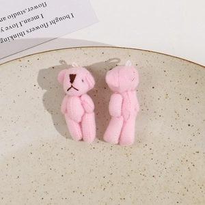 Detail of pink plush teddy bear pendants with white loops on a beige ceramic plate
