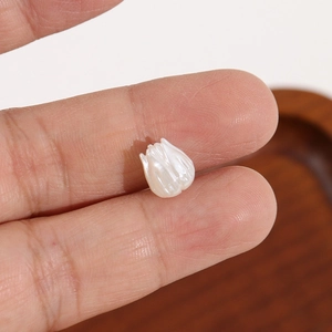Détail macro d'une perle tulipe blanche nacrée tenue par la main pour montrer l'échelle