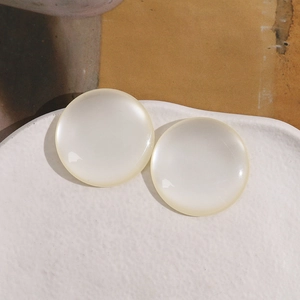 Pair of cream white round resin earrings with pearl-like luster on ceramic tray
