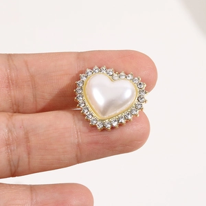 Dettaglio macro di un accessorio a cuore con perla, strass scintillanti e base dorata