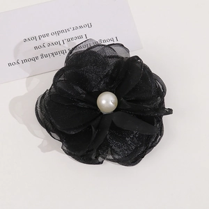 Detail of a black mesh flower hair clip featuring a white pearl center with shimmer