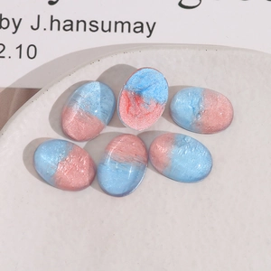 Macro shot of 6 pink and blue resin oval charms with pearlescent finish in a white dish