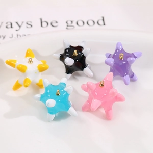 Detail of colorful star-shaped sea urchin pendants with gold rings in a white tray
