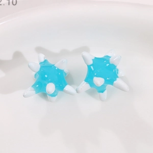 Macro shot of blue resin sea urchin star earrings with white accents on white dish