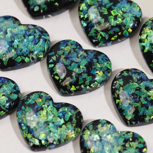 Macro shot of black heart resin charms with vibrant green and blue aurora glitter flakes