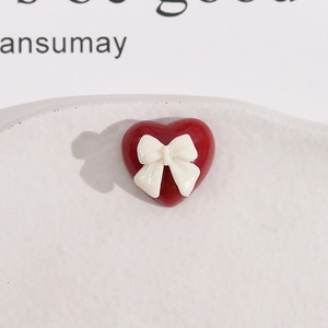 Détail d'une breloque cœur rouge en résine avec un nœud blanc sur un plateau blanc