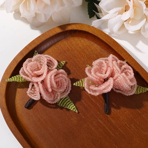 Detail view of handcrafted pink beaded rose with green leaves on dark wooden tray