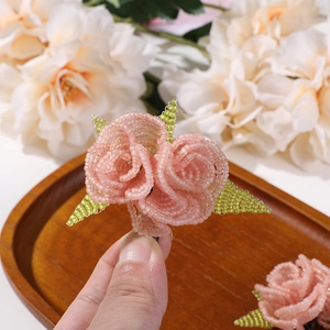 Close-up of handmade pink beaded rose with green leaves for hair accessories and DIY crafts