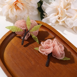 Detail of handmade beaded peach flower brooches with pink glass beads and green leaves