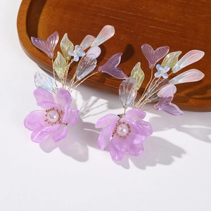 Détail de boucles d'oreilles fleurs en résine violette faites main avec perles et fil doré