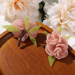 Handmade beaded pink flower and green leaf brooch set on a rustic wooden tray