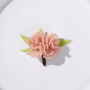 Macro view of a handmade pink beaded rose brooch with light green leaves on a white tray