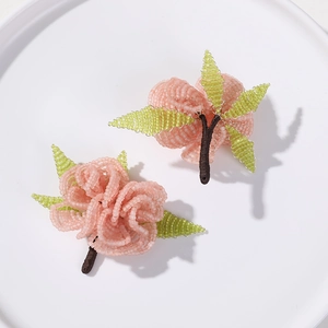 Close-up of handmade pink beaded rose hair pins with green leaves on white plate