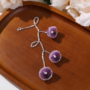 Details von handgefertigten Perlenohrringen mit lila Fächerblüten auf einem Holztablett